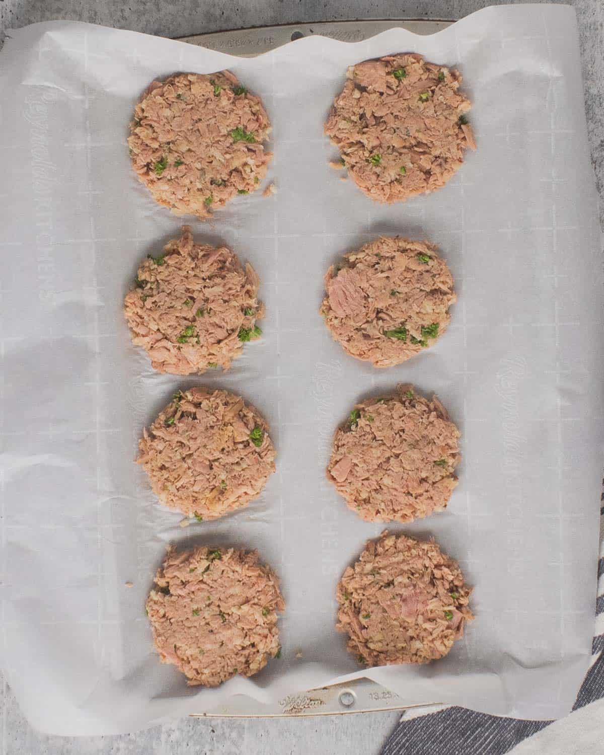 Tuna cakes formed on a lined parchment paper baking sheet.