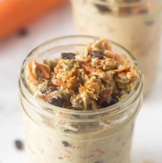 two mason jars with carrot cake overnight oats inside and a carrot in the background.