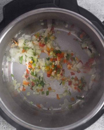 a top view of an instant pot with sautéed onions, garlic, sweet peppers and culantro