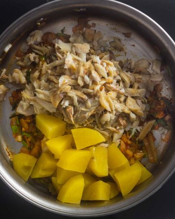 vista superior de sartén con vegetales salteados, agregando bacalao y papas