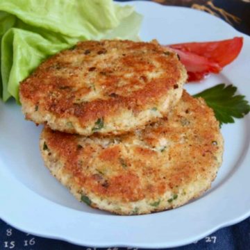 Two salmon patties served on a plate over lettuce.