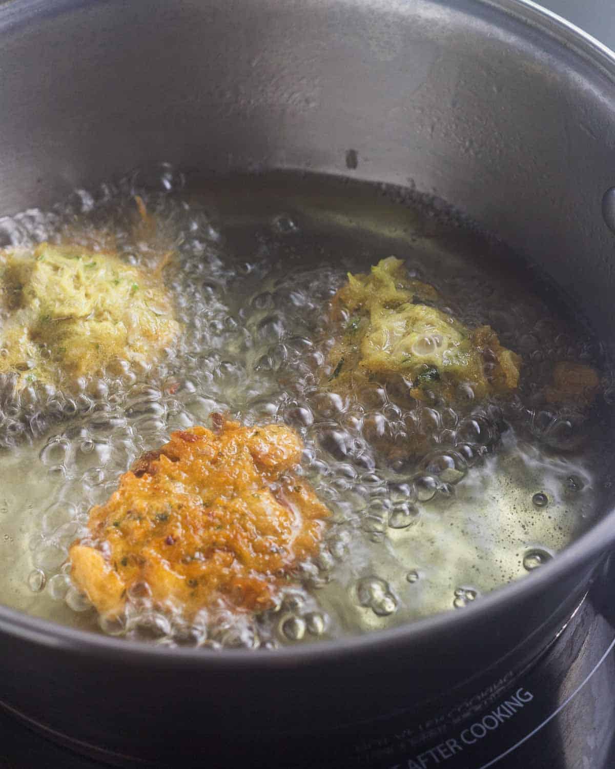 Three cod fritters frying in oil.