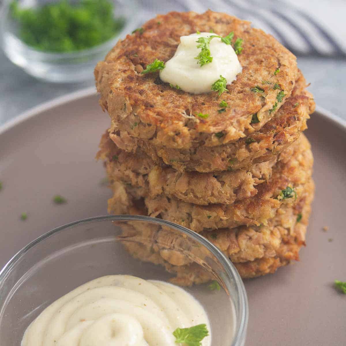 A stack of six tuna patties with a dollop of tartar sauce on a plate.