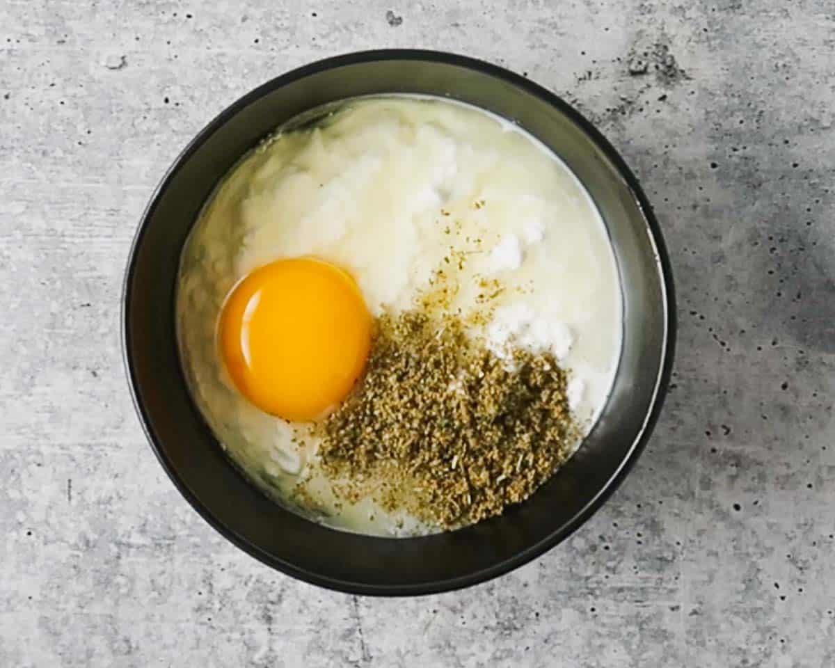 A bowl with cottage cheese, Italian seasoning and an egg before mixing.