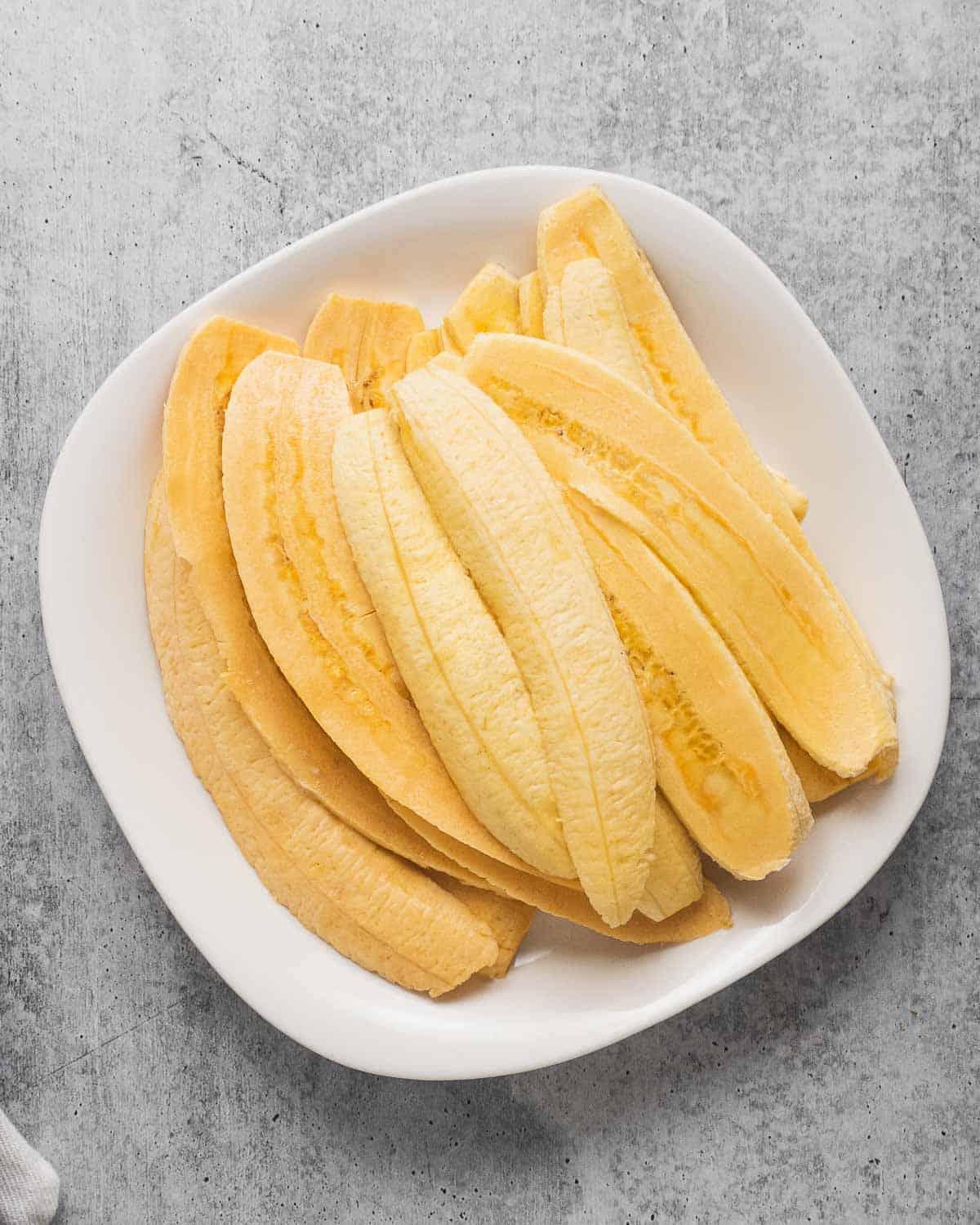 Raw sliced plantain strips on a white plate.