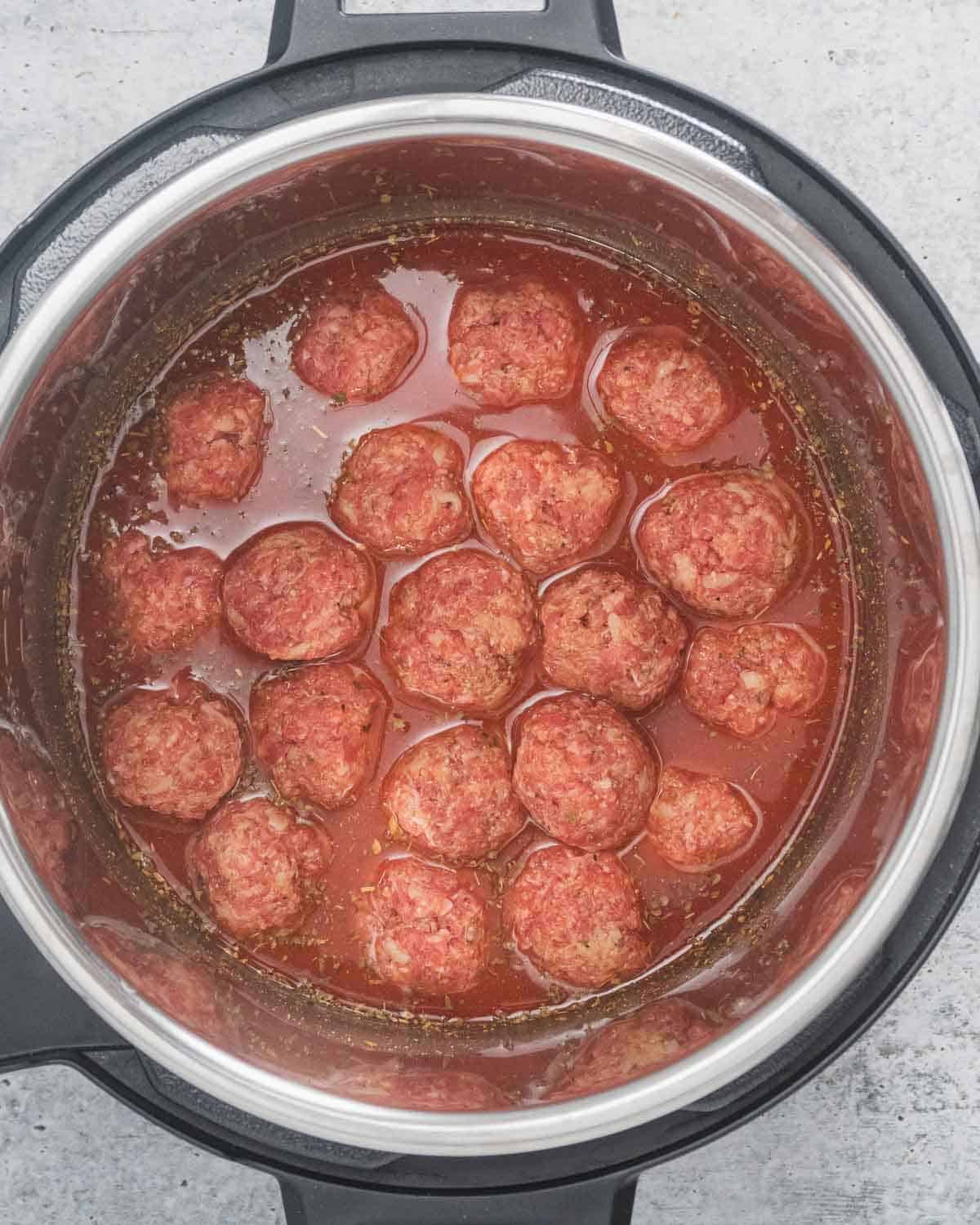 Raw meatballs in sauce inside an Instant Pot.
