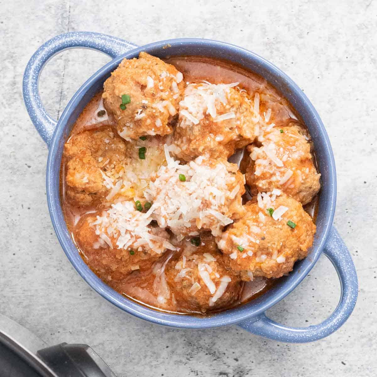 A bowl with meatballs in sauce garnished with parmesan cheese.