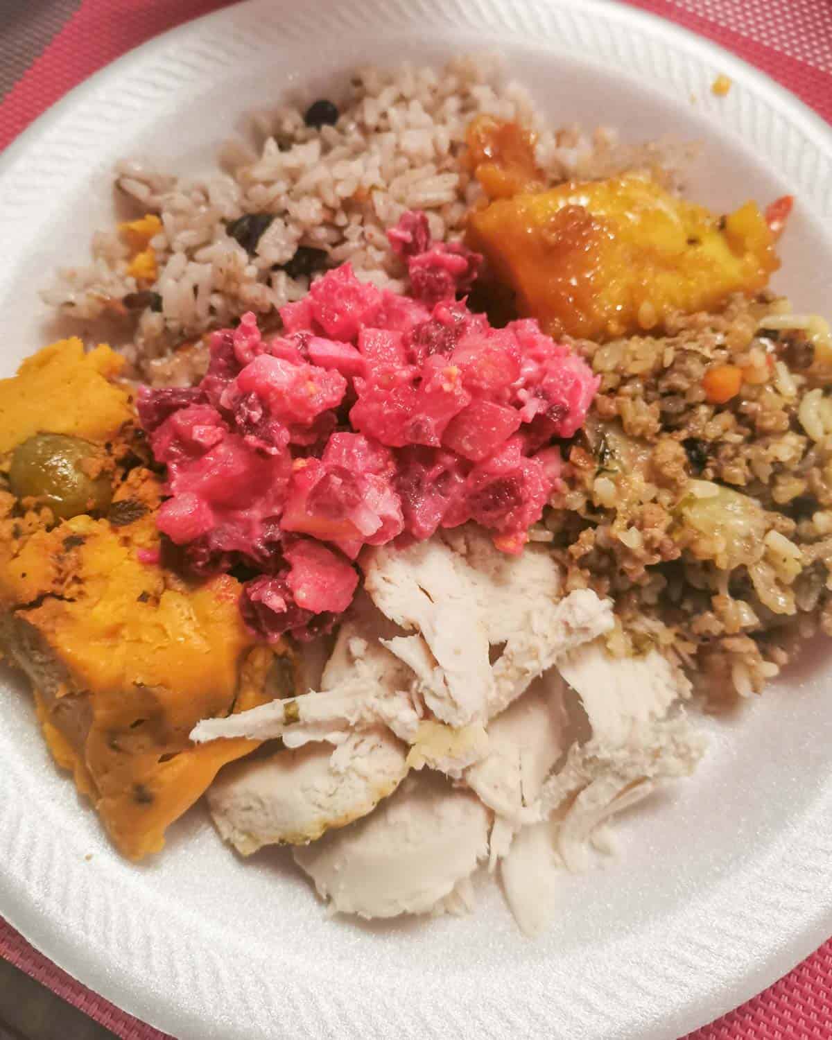 A plate with rice with pigeon peas, tamal, turkey, stuffing, platano en tentacion, and potato and beets salad.