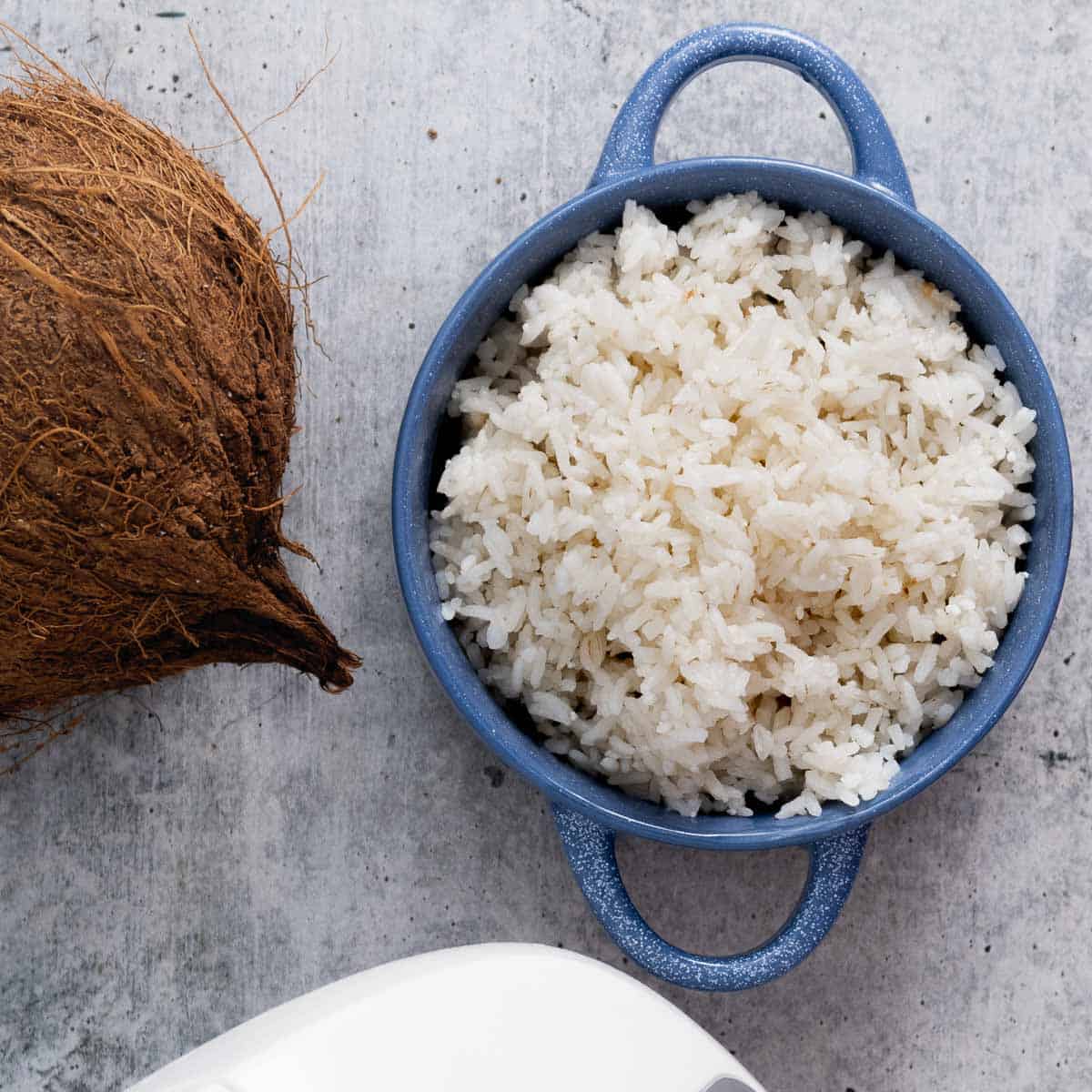 A top view of a bowl with cooked coconut rice in a bowl and a coconut on the side.
