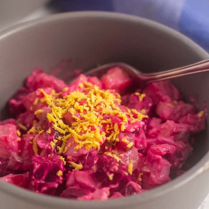 A closeup view of a Panamanian potato and beets salad in a bowl and garnished with grated egg yolk.