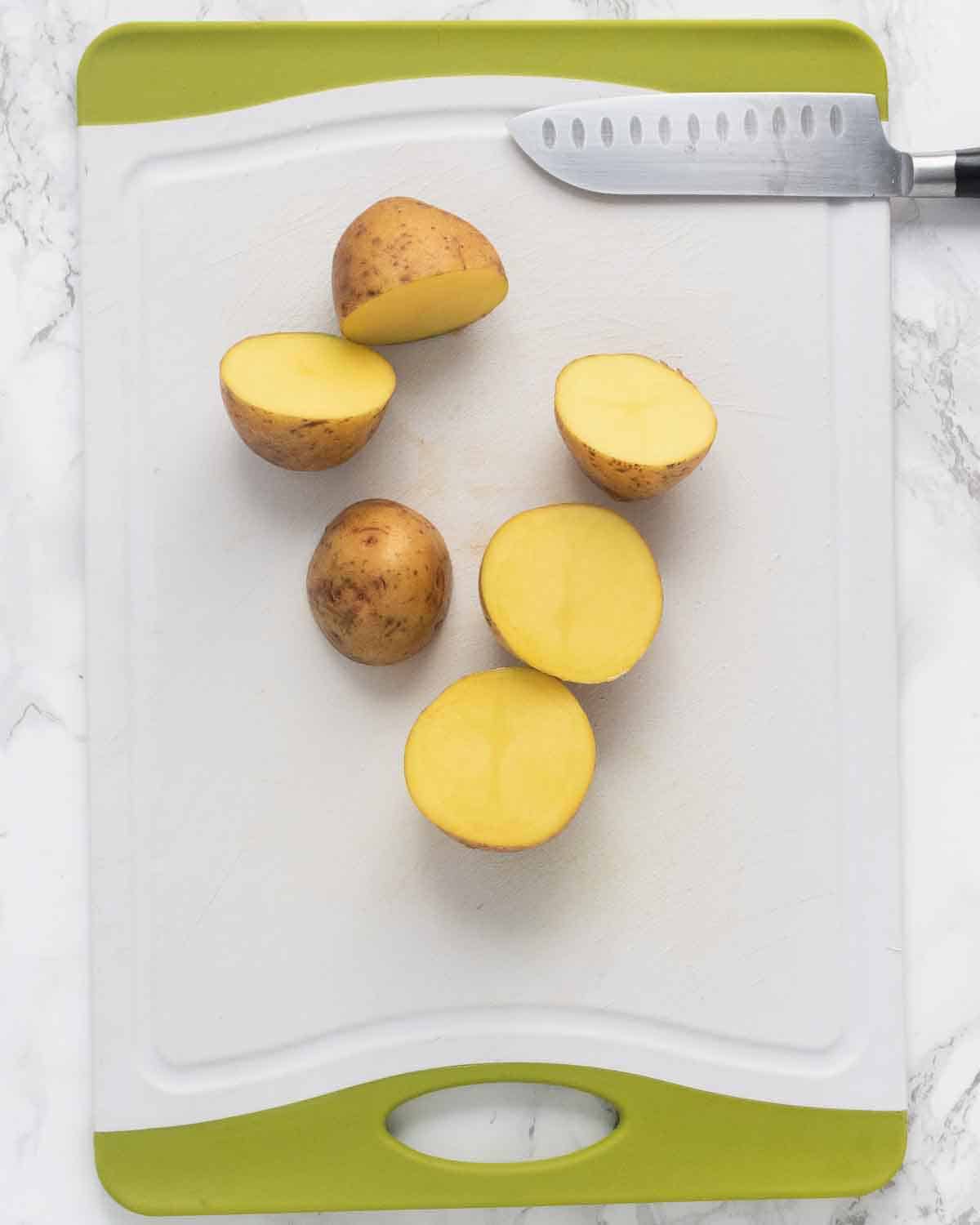 Three Yukon Gold potatoes halved on a chopping board.