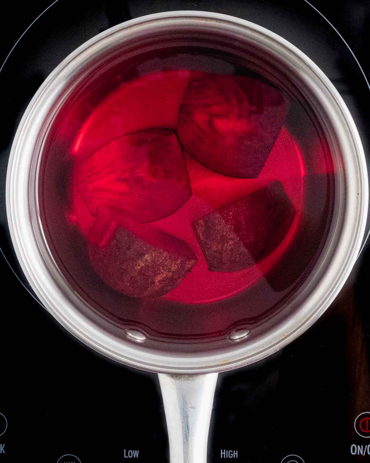 A top view of a saucepan with a quartered beet with water before cooking.