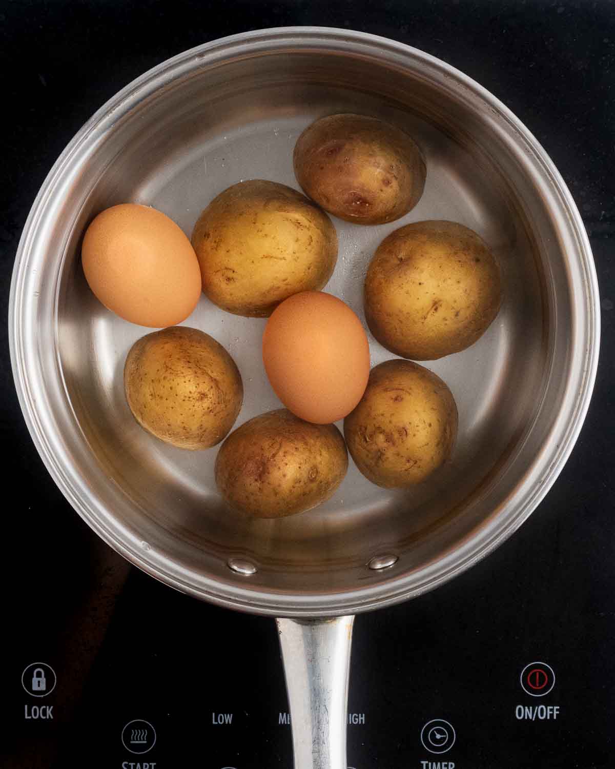A medium saucepan with halved potatoes and two eggs covered with water before cooking.