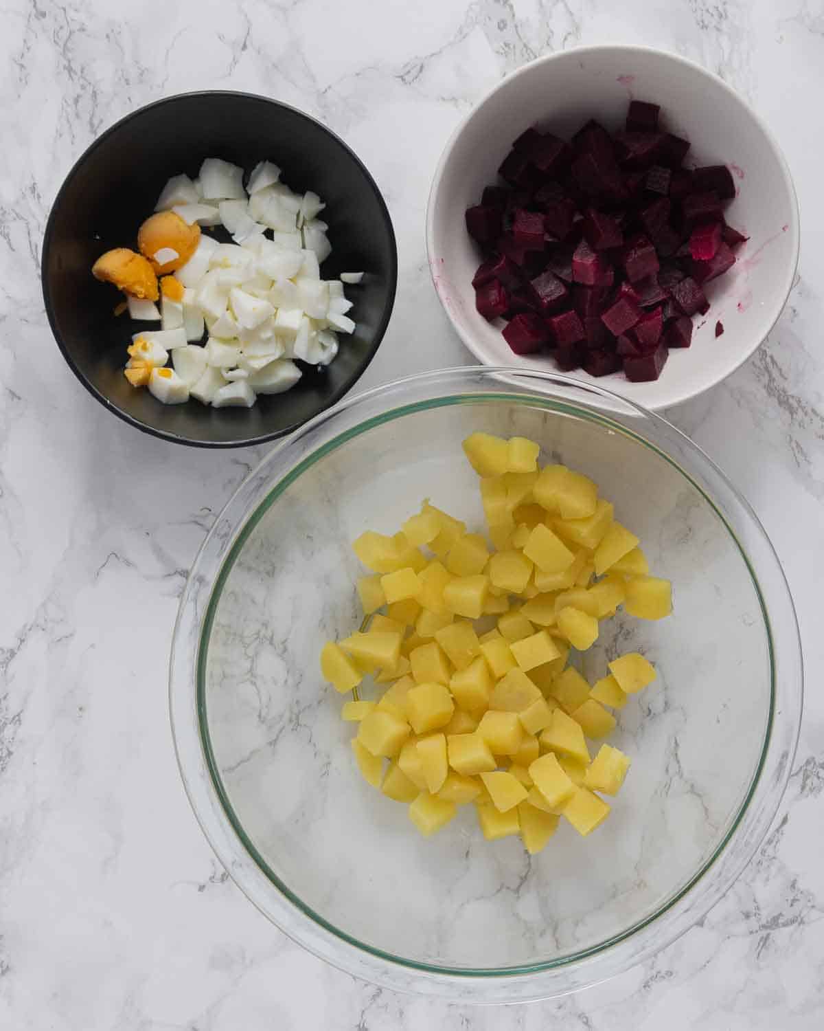 Three bowls, one with chopped beets, chopped eggs, and chopped potatoes.