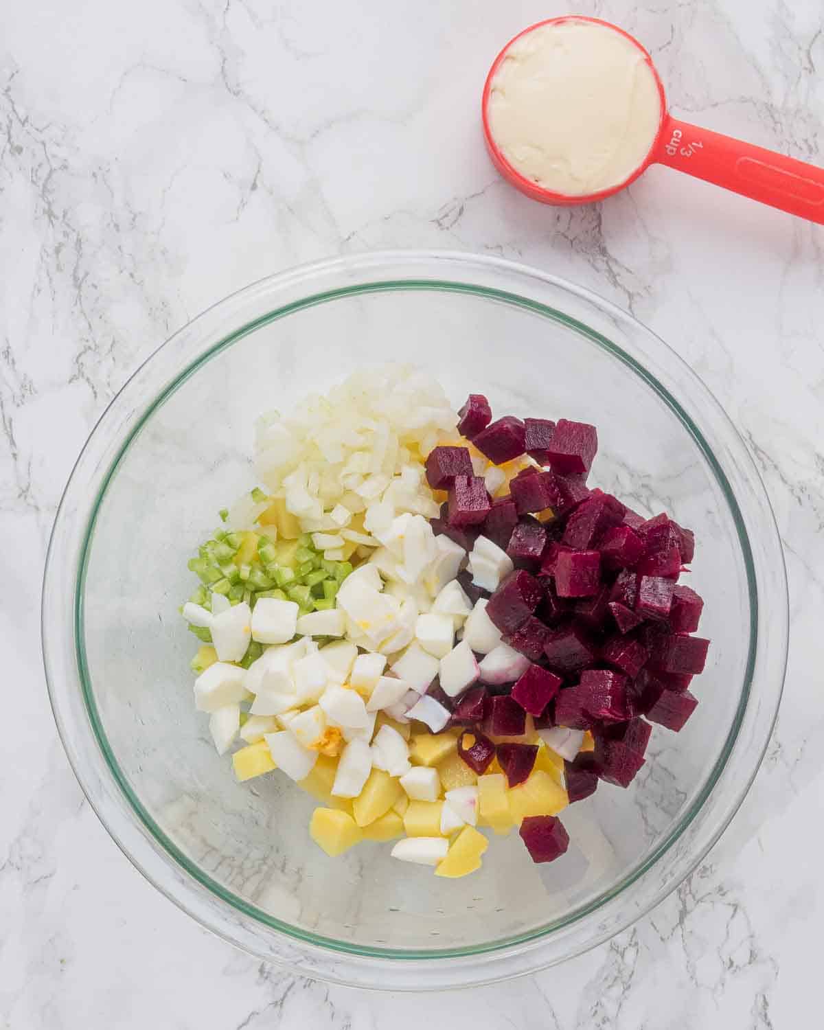 A large mixing bowl with chopped potatoes, beets, onion, celery and eggs.