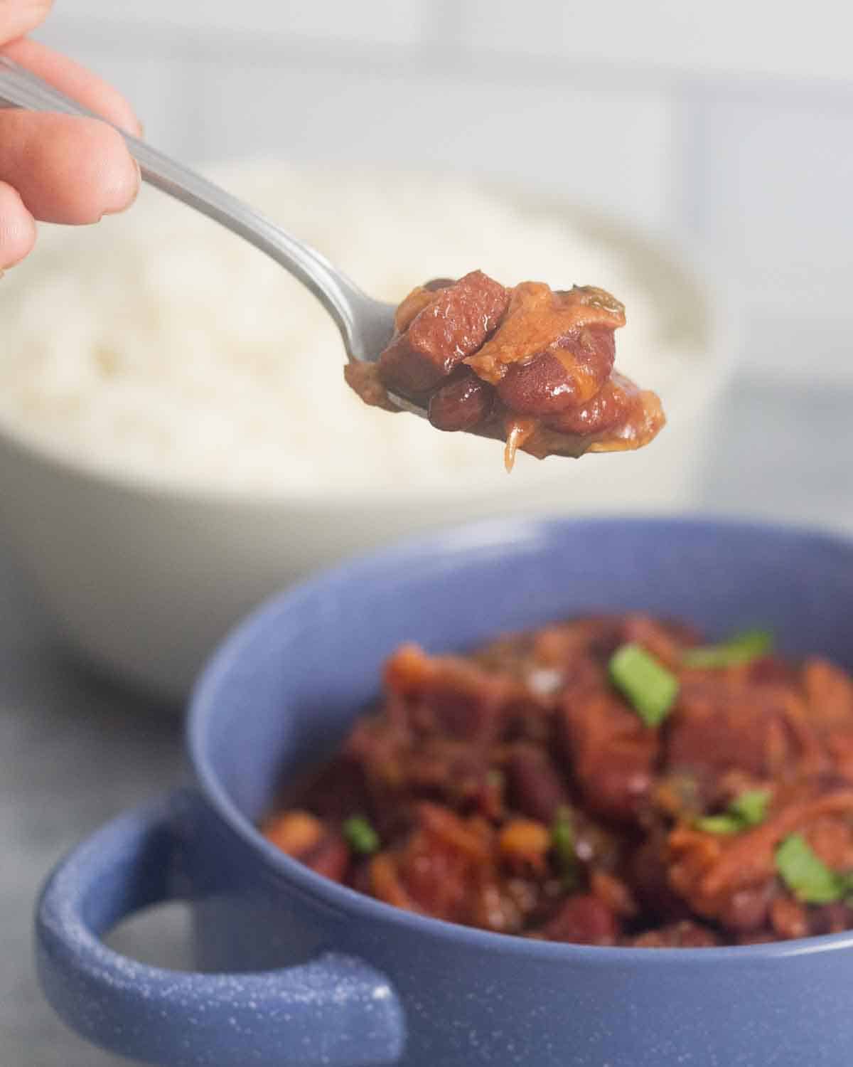 A closeup of a spoon with cooked red beans and ham.