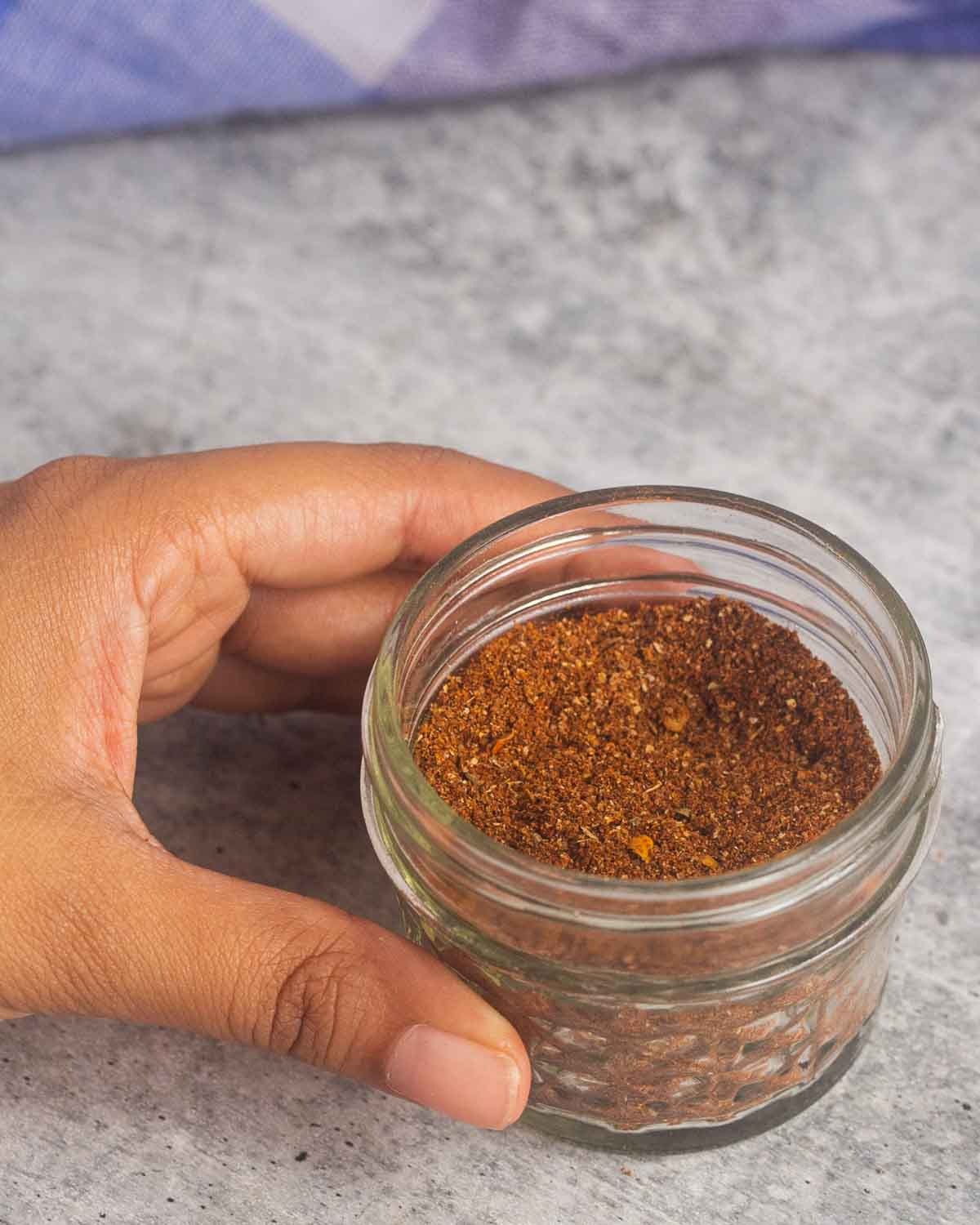 A woman hand holding 4 ounce mason jar with chili con carne spice mix in it.