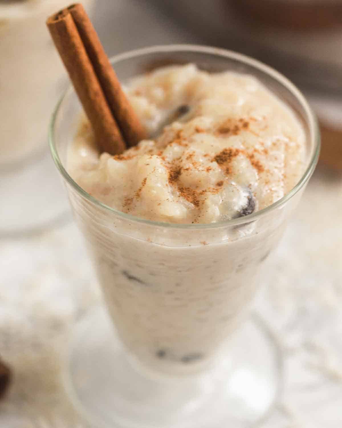 Close up of a glass with rice pudding, a cinnamon stick and ground cinnamon sprinkled on top.