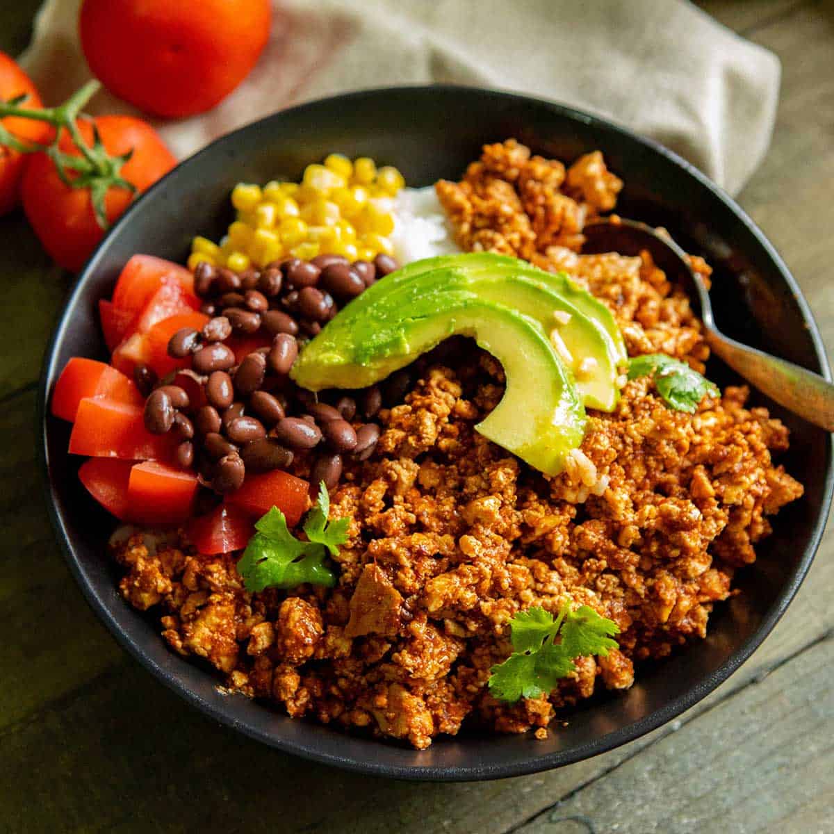 A bowl with sofritas, beans, chopped tomatoes, corn, rice and avocado.