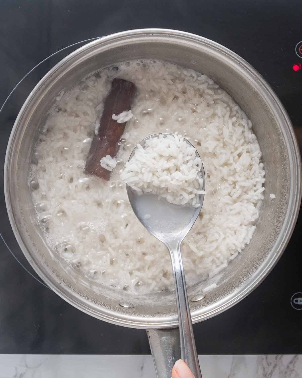 A pot with cooked rice and a cinnamon stick.