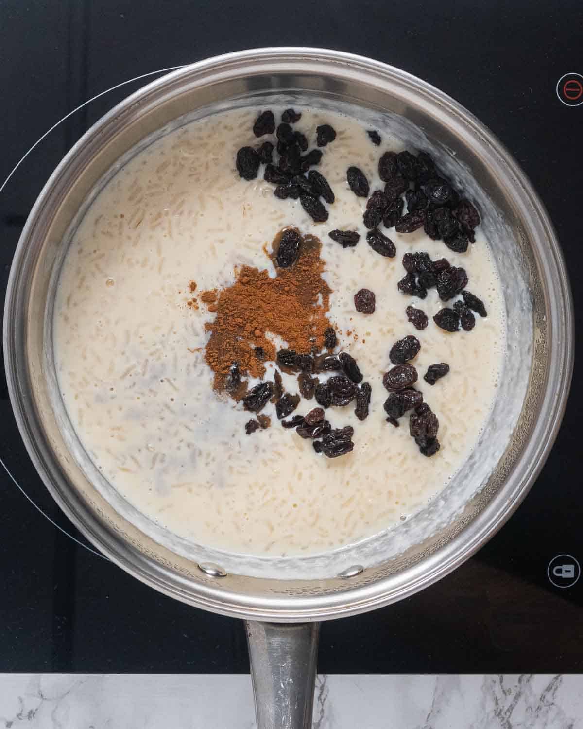 A pot with cooked rice, milk, ground cinnamon, raisins and vanilla extract.