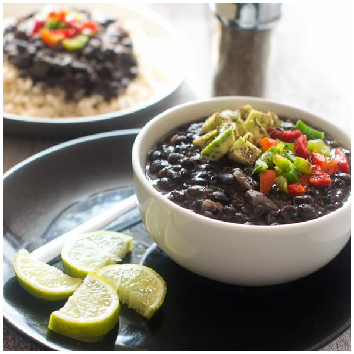 A bowl with cooked black beans topped with diced avocado and green and red bell peppers.