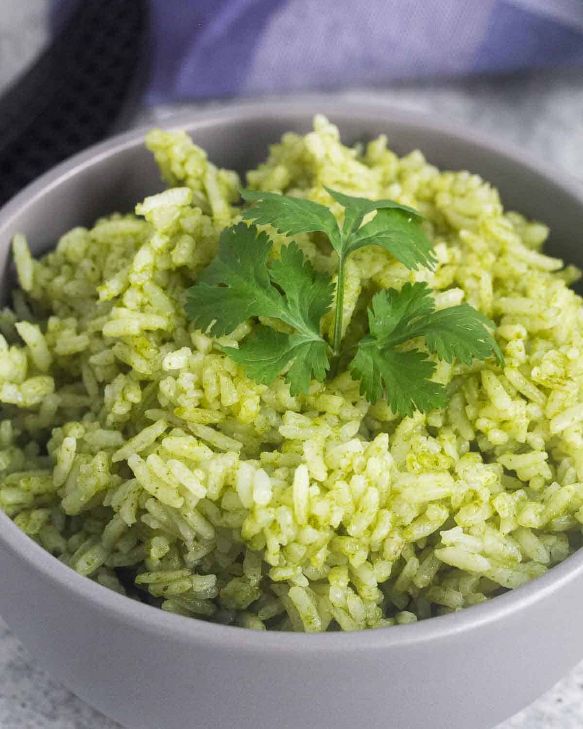 A closeup of a bowl with arroz verde (green rice) and cilantro leaves as garnish.