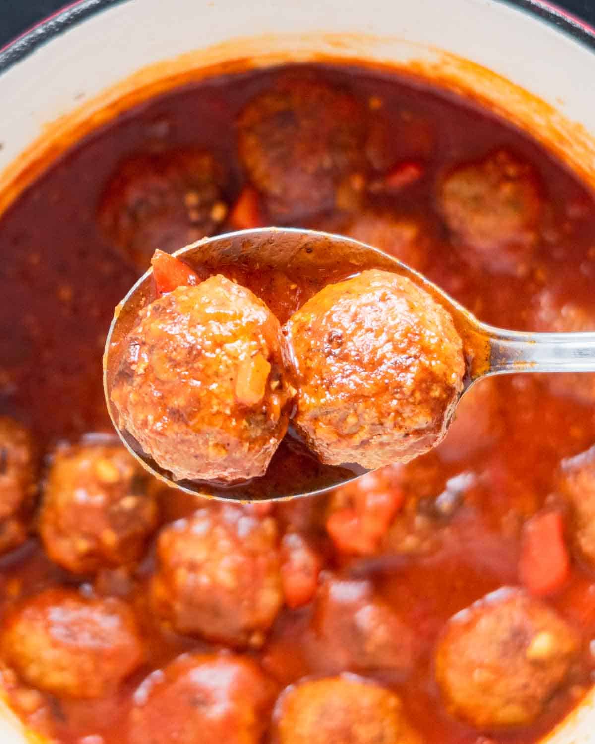 A closeup of a spoon with two meatballs over a Dutch oven.