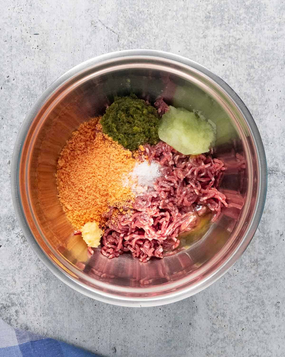 A stainless steel mixing bowl with meatballs ingredients before mixing.