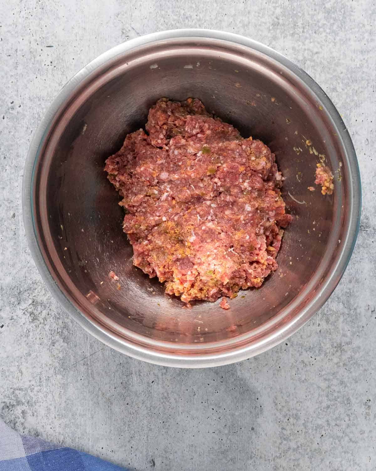 Mixed meatball mixture in a stainless steel mixing bowl.