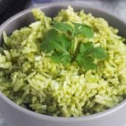 A closeup of a bowl with green rice and cilantro leaves as garnish.