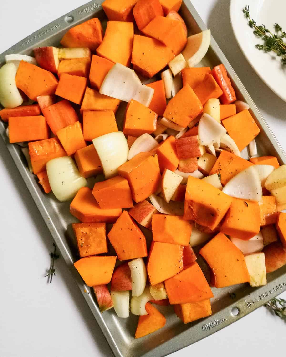 Seasoned and chopped pumpkin, carrots, onion, and apple on a baking sheet before baking.