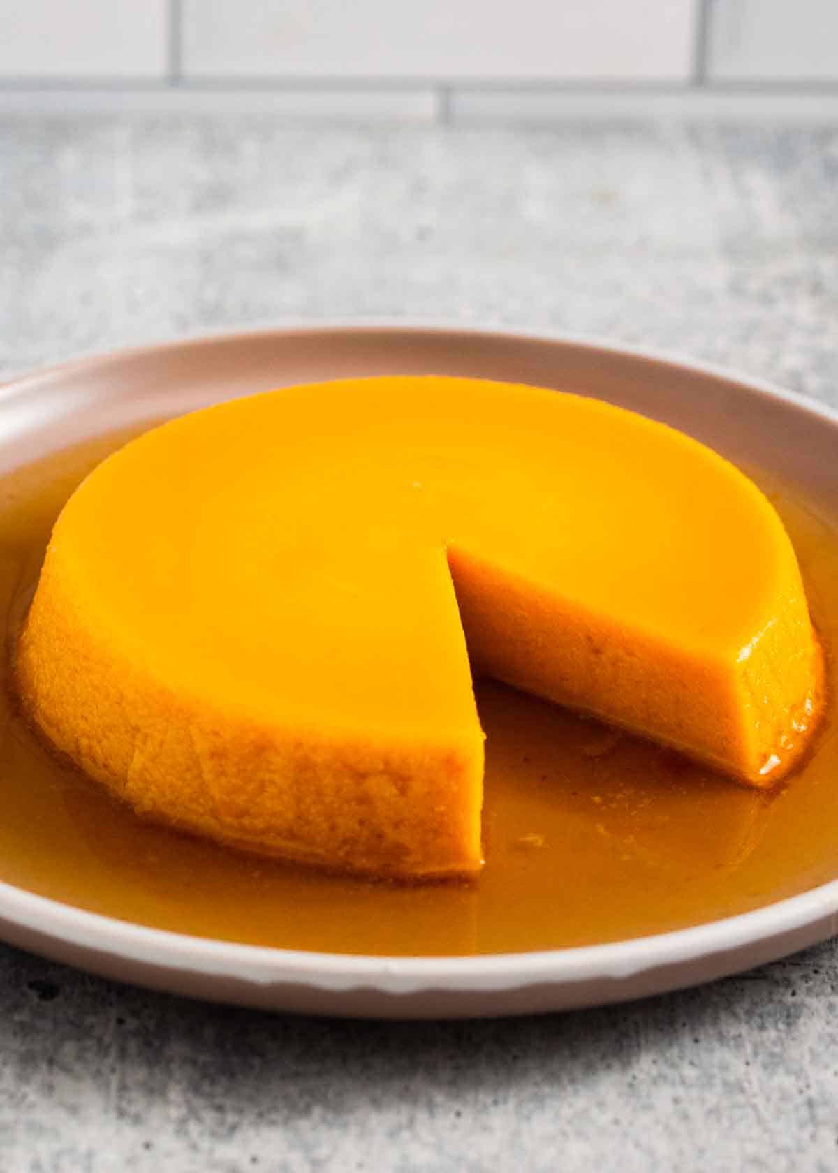 Baked pumpkin flan served on a plate with a slice taken out.