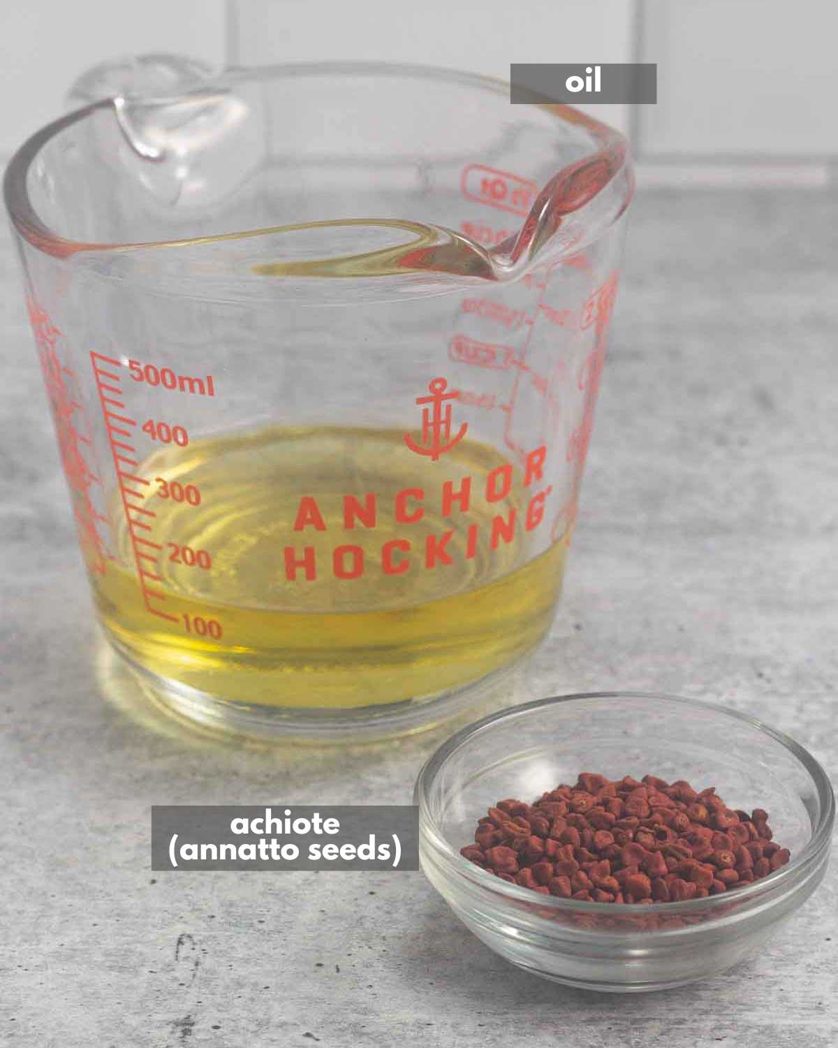 A liquid measuring cup with oil and a small bowl with annatto seeds.