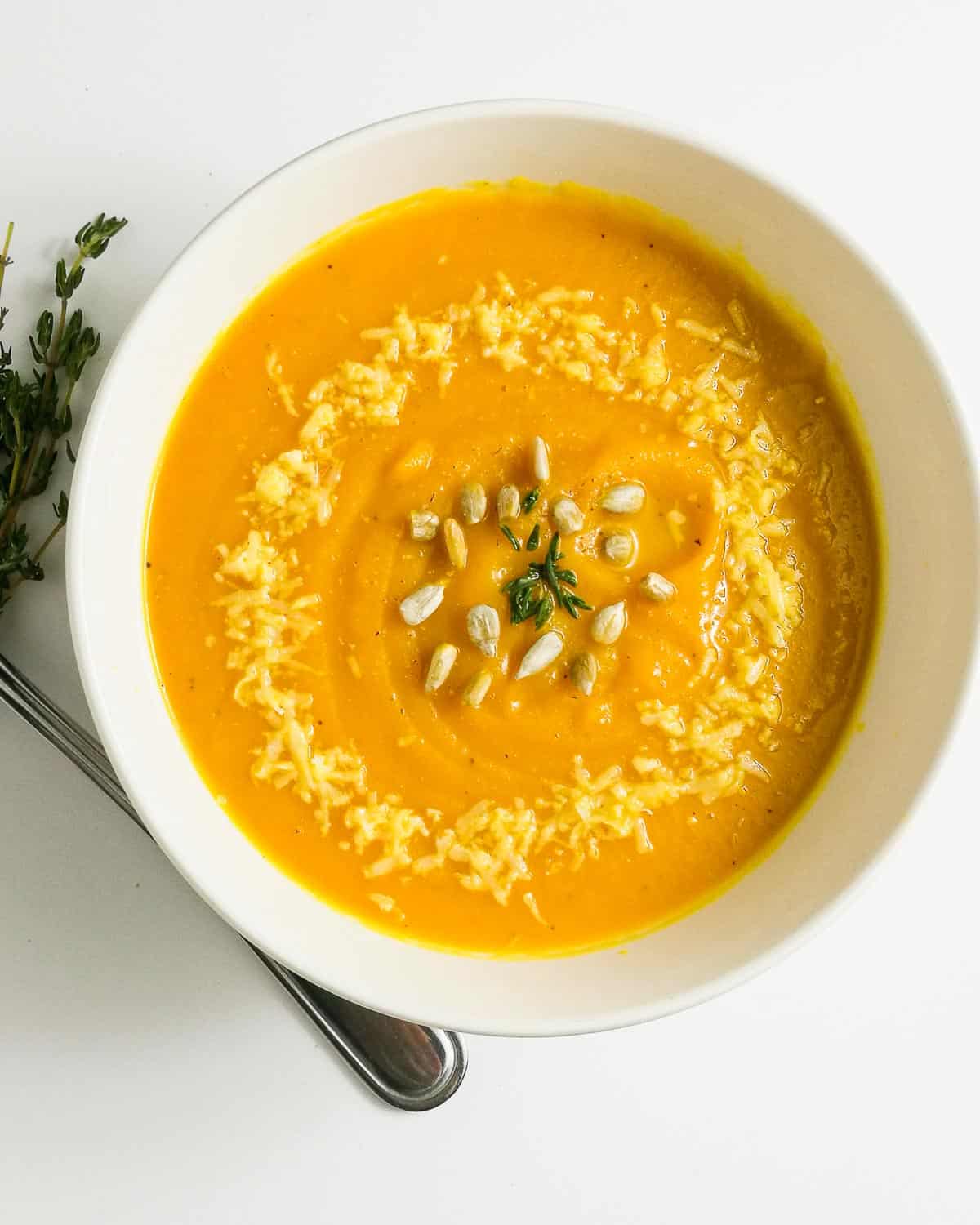 A bowl of roasted pumpkin soup without cream garnished with parmesan cheese and thyme.