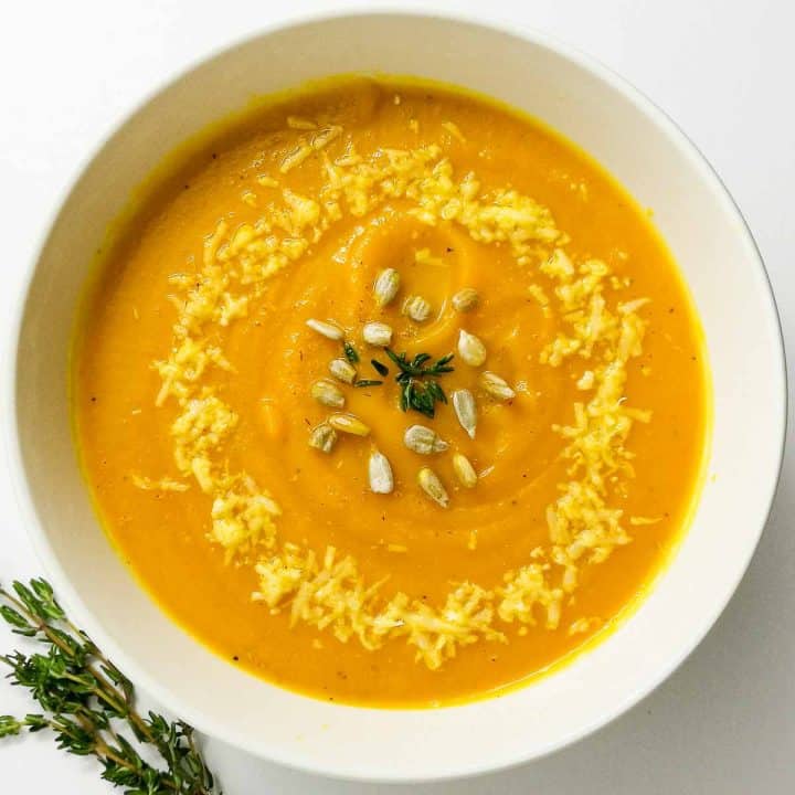A bowl of roasted pumpkin soup without cream garnished with parmesan cheese and thyme.