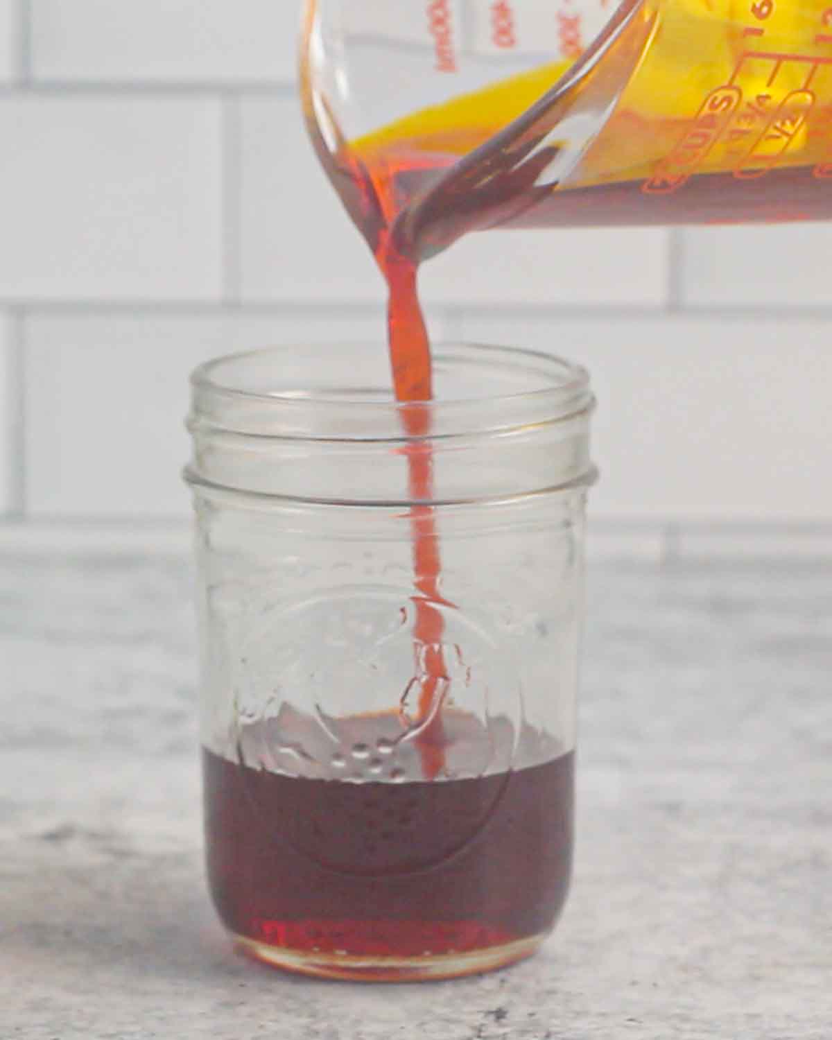 Pouring strained annatto oil into a mason jar.