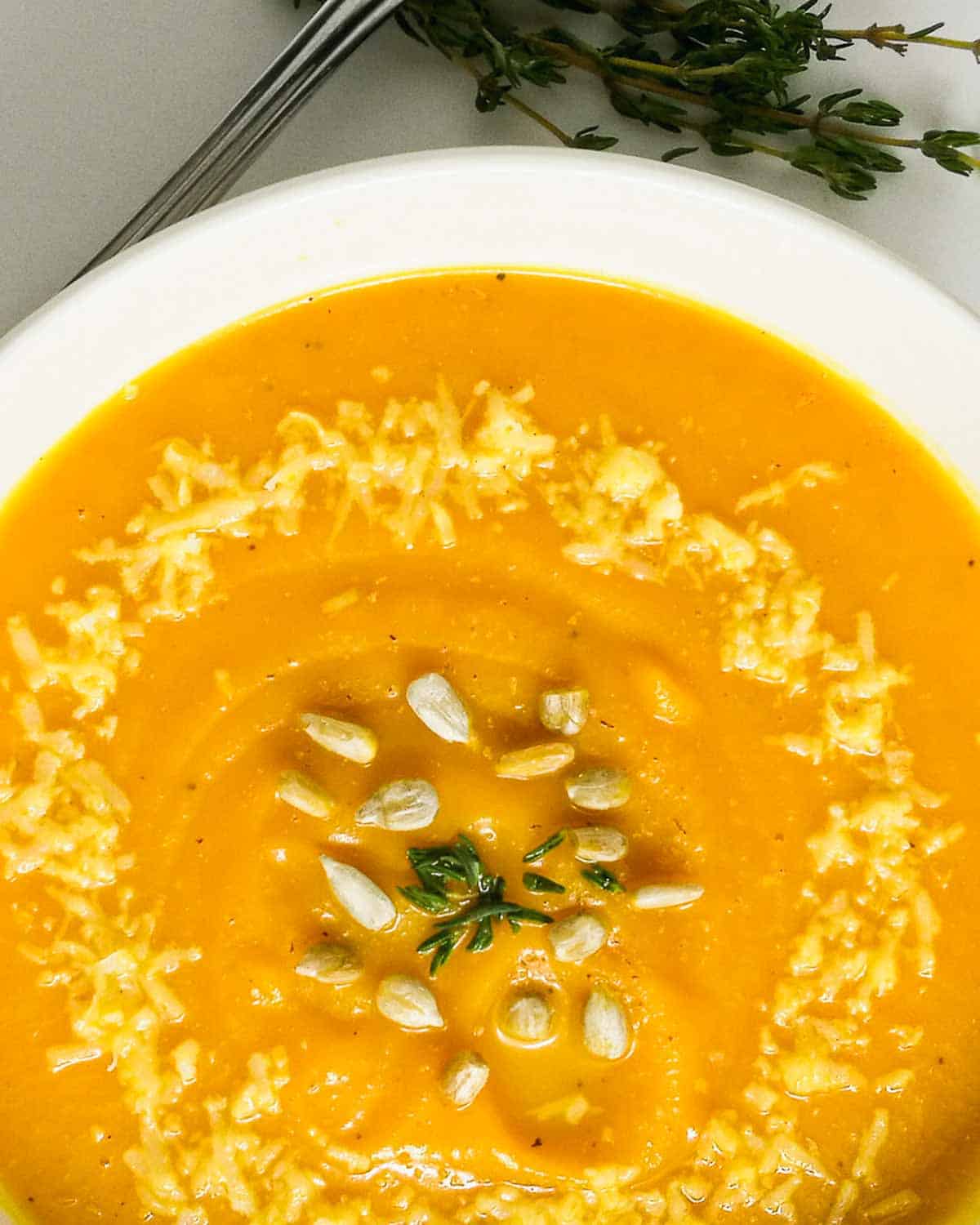 Closeup of a bowl of roasted pumpkin soup without cream garnished with parmesan cheese and thyme.