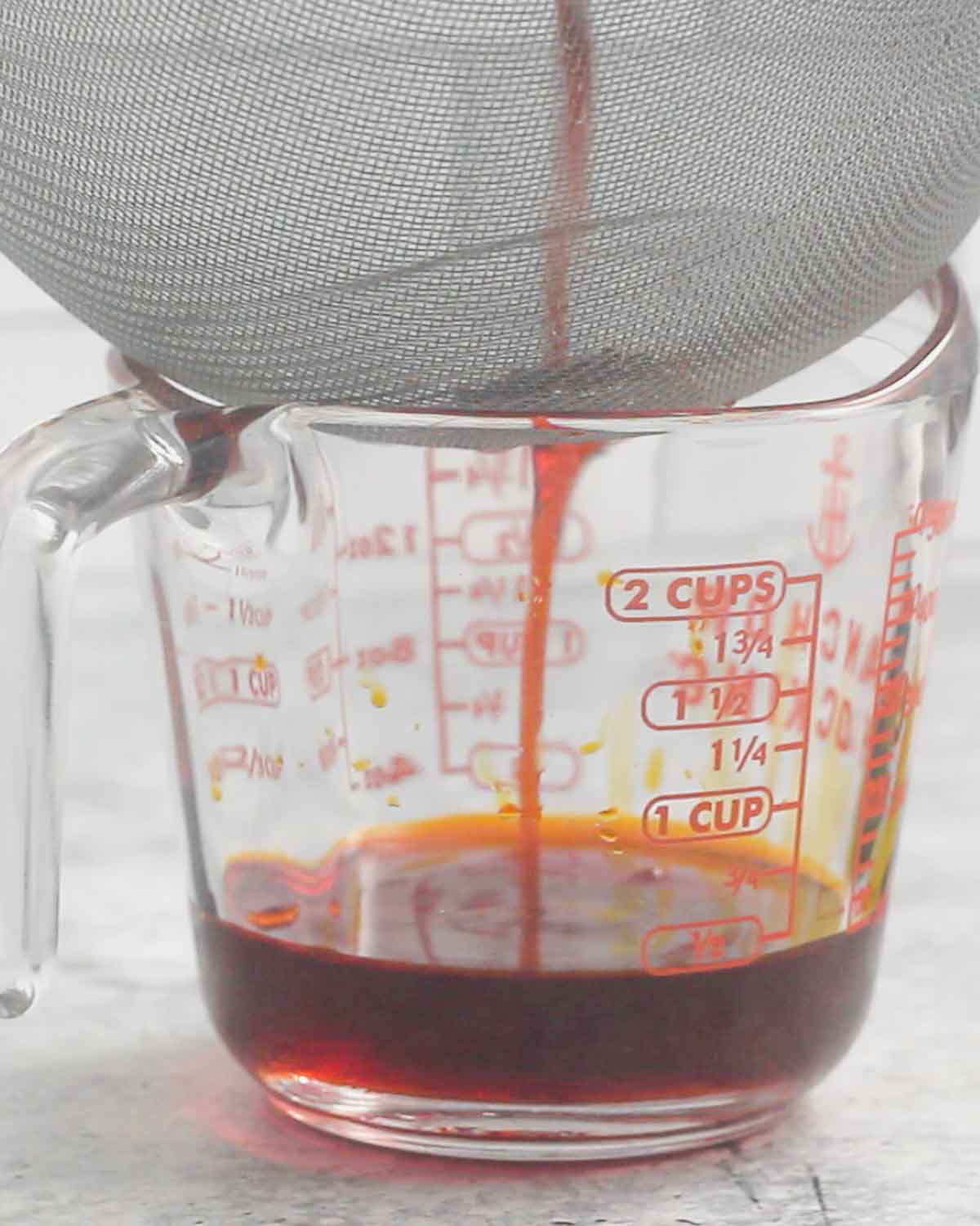Straining the achiote oil in a liquid measuring cup.